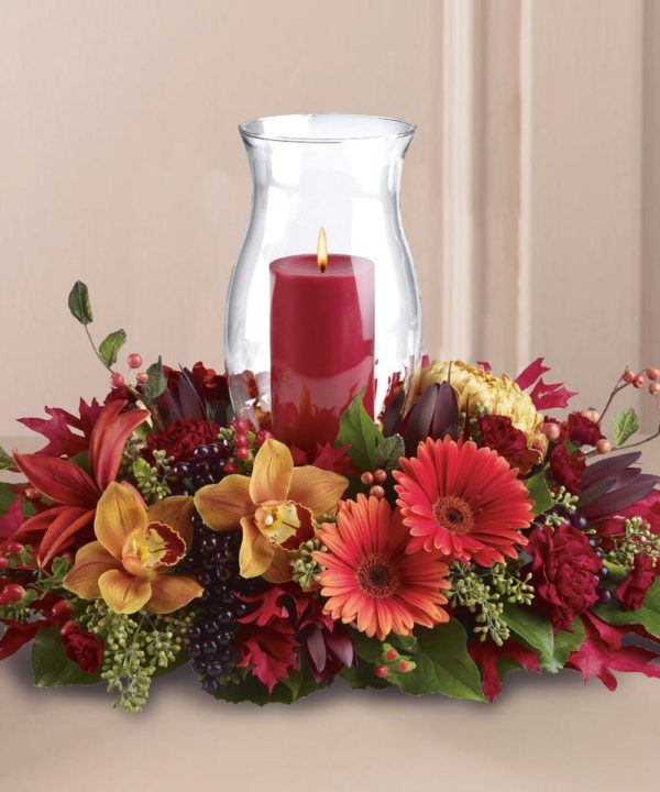 Red candle amongst red and tan and green fall flowers