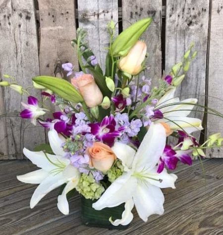 A glass cube vase filled with stargazer lilies, rose, orchids and more! Send our floral embrace to let that special someone know just how much you care.