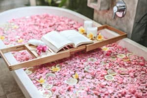 Bath with pink flower petals, fruit, candles, and open book